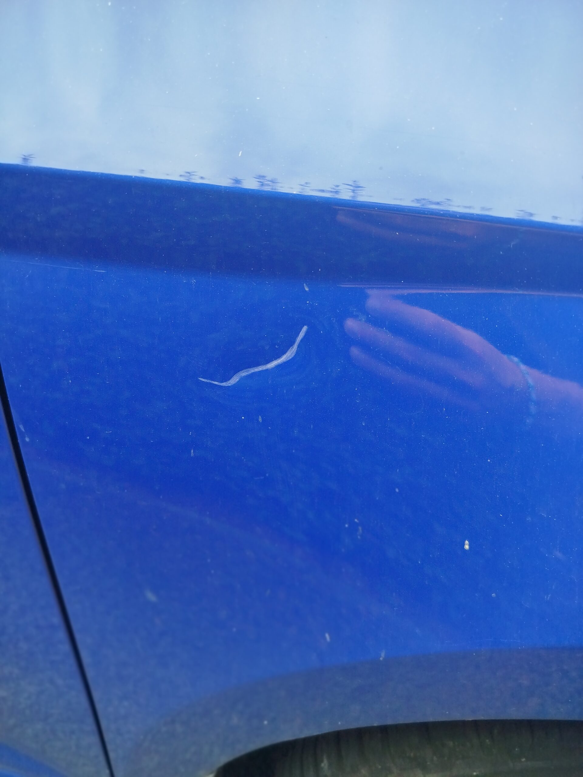 Nahaufnahme von einem Kratzer im Lack eines Autos.